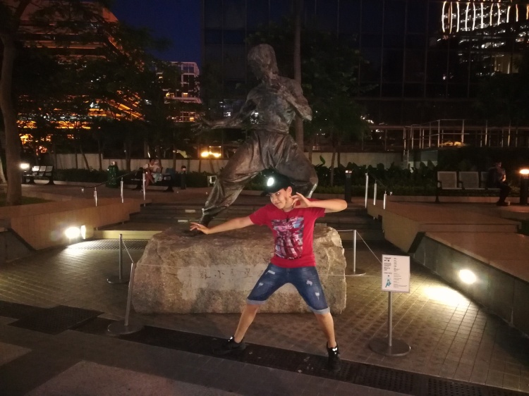 Estátua do Bruce Lee, adolescente tentando imitar a pose da estátua, noite